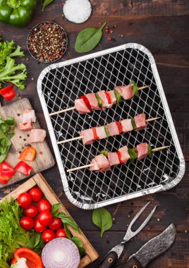 Çatal ve bıçak ile ahşap arka planda taze sebzeler ile tek kullanımlık kömür BBQ ızgara üzerinde Paprika ile ham domuz kebap. Tuz ve biber ile marul ve Paprika ve kiraz domates. Üst görünüm