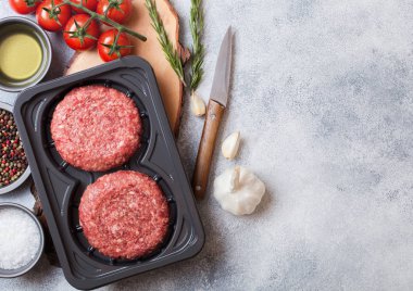 Baharat ve otlar ile ham kıyılmış ev yapımı sığır Burger ile plastik tepsi. Metin alanı ile üst görünüm. Domates tuz ve biber ile mutfak masası arka planda.