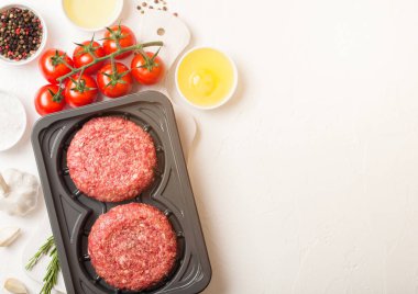 Baharat ve otlar ile ham kıyılmış ev yapımı sığır Burger ile plastik tepsi. Üst görünüm ve domates tuz ve biber ile beyaz mutfak masa arka plan üstünde metin için alan.