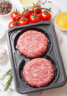 Baharat ve otlar ile ham kıyılmış ev yapımı sığır Burger ile plastik tepsi. Üst görünüm. Domates tuzu ve biber ile beyaz mutfak masa arka plan üstünde.
