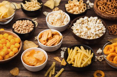 Tüm klasik patates atıştırmalıkları, fıstık, patlamış mısır ve soğan halkaları ve ahşap arka planda kase plakaları tuzlu kraker. Cips ve patates cipsi, nachos ve peynir topları ile cipsler ile Twirls.