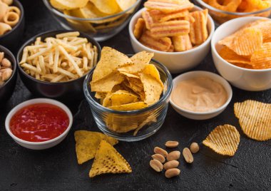 Fıstık, patlamış mısır ve soğan halkaları ve siyah arka planda kase plakaları tuzlu kraker ile tüm klasik patates atıştırmalıkları. Cips ve patates cipsi, nachos ve peynir topları ile cipsler ile Twirls.