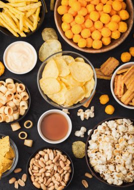 Fıstık, patlamış mısır ve soğan halkaları ve siyah arka planda kase plakaları tuzlu kraker ile tüm klasik patates atıştırmalıkları. Cips ve patates cipsi, nachos ve peynir topları ile cipsler ile Twirls.