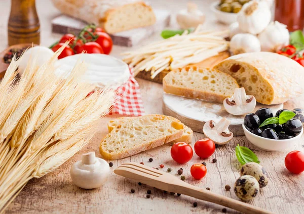 Pane di grano fatto in casa con uova di quaglia e grano crudo e pomodori freschi su sfondo di legno. Cibo classico italiano del villaggio. Olive all'aglio, nere e verdi. spatola di legno — Foto Stock