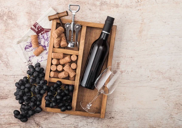 Flaska rött vin och tomt glas med mörka druvor med korkar och öppnare insida Vintage trälåda på trä bakgrund med linne handduk. Uppifrån och — Stockfoto