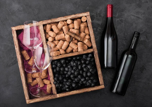 赤い布で暗い木製の背景にヴィンテージの木製の箱の中にコルクとコルクとコルクネジと空のメガネと暗いブドウと木の上の赤ワインのボトル。トップビュー — ストック写真