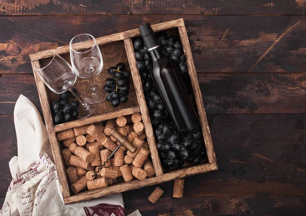 豪华一瓶红酒和空玻璃杯,带黑葡萄,软木塞和软木塞,在深色木制背景与亚麻毛巾的复古木箱内。顶部视图 — 图库照片