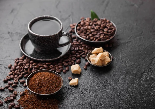 검은 배경에 커피 나무 잎이있는 지팡이 설탕 큐브가있는 콩과 분쇄 분말을 곁들인 신선한 생 유기농 커피 컵. 맨 위 보기 — 스톡 사진