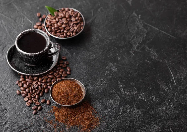 Tasse de café bio cru frais avec haricots et poudre moulue avec feuille de caféier sur fond noir. Vue du dessus — Photo
