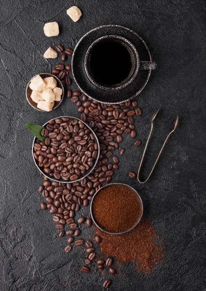 Cup of fresh raw organic coffee with beans and ground powder with cane sugar cubes with coffee tree leaf on black background. Top view — Stock Photo, Image