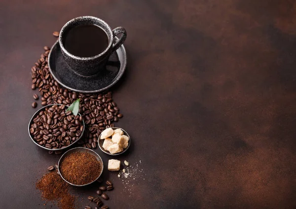 Cup of fresh raw organic coffee with beans and ground powder with cane sugar cubes with coffee tree leaf on brown background. Space for text. — Stock Photo, Image