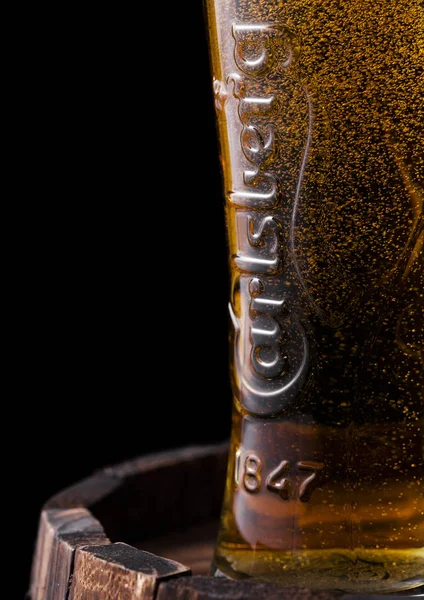 LONDRES, Reino Unido - 27 DE ABRIL DE 2018: Original vaso de cerveza Carlsberg encima del viejo barril de madera con rocío y burbujas . Imagen De Stock