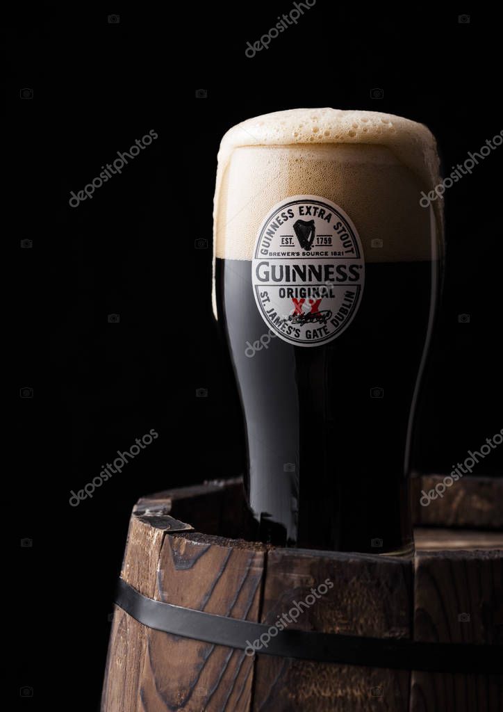 LONDON, UK - APRIL 27, 2018: Original glass of Guinness original stout beer on top of old wooden barrel. Guinness beer has been produced since 1759 in Dublin, Ireland.