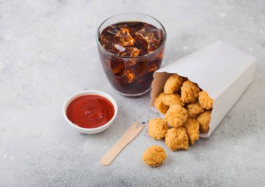 Hafif arka planda ketçap ve kola bardağı ile fast food yemek için beyaz kağıt kapta Gevrek güney tavuk patlamış mısır ısırıkları. 