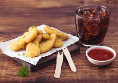 Ahşap arka plan üzerinde kola ve ketçap cam ile doğrama tahtası üzerinde Tereyağlı tavuk nuggets. 