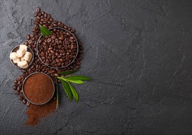 Zemin tozu ve siyah arka plan üzerinde kahve trea yaprağı ile şeker kamışı küpleri ile taze çiğ organik kahve çekirdekleri.