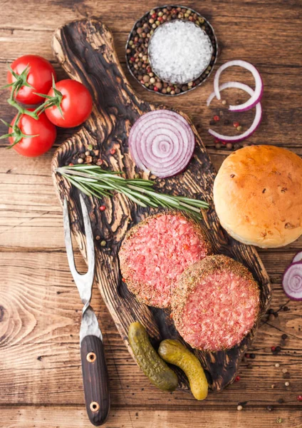 Burgers de bœuf au poivre cru haché frais sur planche à découper vintage avec petits pains oignon et tomates sur fond en bois. Vue du dessus — Photo
