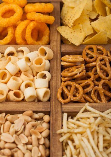 Varios aperitivos en caja de madera vintage. Anillos de cebolla, nachos, cacahuetes salados con palitos de patata y pretzels. Adecuado para cerveza y bebidas gaseosas. Macro — Foto de Stock