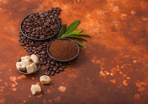 Свежий сырой органический кофе в зернах с молотым порошком и тростниковым сахаром кубики с листьями дерева кофе на светлом коричневом фоне . — стоковое фото