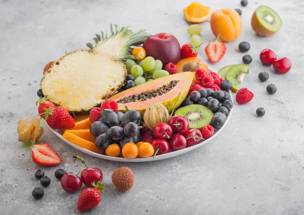 新鲜的生有机夏季浆果和异国情调的水果在白色板在光的背景。菠萝,木瓜,葡萄,花蜜,橙子,杏,奇异果,梨,芦荟,樱桃和香菜. — 图库照片