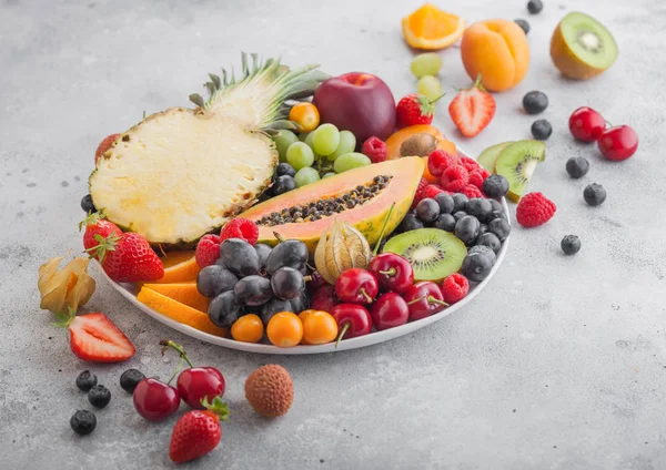 Frescas bayas de verano orgánicas crudas y frutas exóticas en plato blanco sobre fondo claro. Piña, papaya, uvas, nectarina, naranja, albaricoque, kiwi, pera, lichis, cereza y physalis . — Foto de Stock