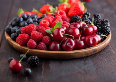 Taze organik böğürtlenler, koyu ahşap masa arka planında yuvarlak ahşap tepside karıştırılır. Ahududu, çilek, yabanmersini, böğürtlen ve kiraz. Makro. Kapat.