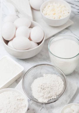 Beyaz mermer arka planda taze süt ürünleri. Süt, un kase, ekşi krema ve süzme peynir ve yumurta bardak. Çelik çırpıcı. Üstte görüntü. 