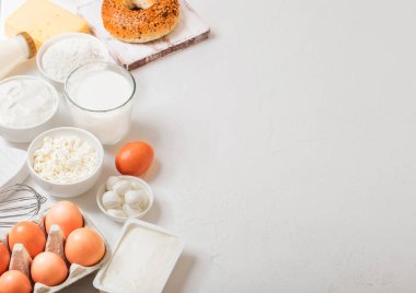 Beyaz masa arka plan üzerinde taze süt ürünleri. Bardak süt, kase ekşi krema ve süzme peynir ve yumurta. Taze pişmiş simit. Çelik çırpma teli. Üstten Görünüm. Metin için yer