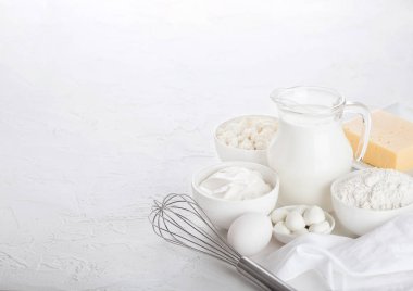 Beyaz masa arka planda taze süt ürünleri. Süt cam kavanoz, ekşi krema kase, süzme peynir ve kabartma un ve mozzarella. Yumurta ve peynir. Çelik çırpıcı. Metin için alan