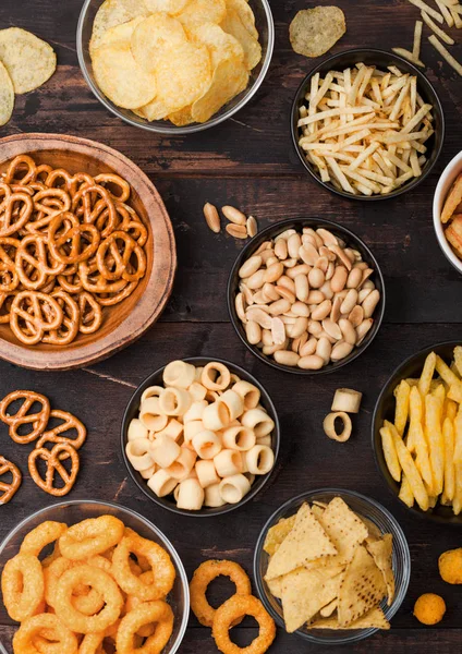 Tüm klasik patates atıştırmalıkları, fıstık, patlamış mısır ve soğan halkaları ve ahşap arka planda kase plakaları tuzlu kraker. Cips ve patates cipsi, nachos ve peynir topları ile cipsler ile Twirls.