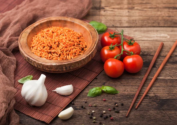 Wooden plate bowl of rice with tomato and basil and garlic and chopsticks on brown bamboo place mat on wooden background with dark cloth. Top view. — Stock Photo, Image