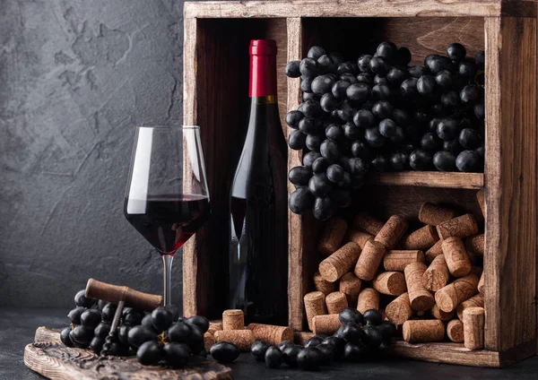 在黑石背景的复古木箱内，有一瓶红葡萄酒，内有深色葡萄和软木塞。典雅的葡萄酒杯，黑板上有软木塞。自然光 — 图库照片