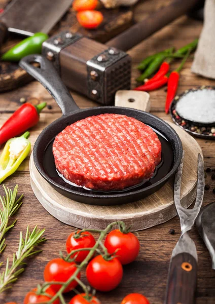 Des agriculteurs frais hachés à la maison grillent des hamburgers de bœuf sur une planche à découper ronde et une poêle avec des épices et des herbes et une hache de viande sur une planche en bois. Huile, ail et tomates . — Photo