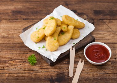 Ahşap arka plan üzerinde ahşap çatal ve ketçap ile doğrama tahtası üzerinde tereyağlı tavuk nuggets.