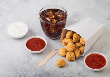 Çıtır çıtır güney tavuk patlamış mısırları ketçaplı fast food yemekleri ve arka planda bir bardak kola için beyaz kağıt konteynırda ısırabilir. Üst görünüm