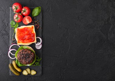 Siyah arka plan üzerinde çörekler soğan ve domates ile taş doğrama tahtası üzerinde Taze ızgara kıyma burger. Tuzlu turşu ve ketçap ile peynir dilimi.