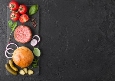Biberli taze et burgeri taştan doğranmış tahtanın üzerinde soğanlı çörekler ve siyah arka planda domatesler. Tuzlu turşu ve fesleğen. Metin için boşluk