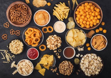 Fıstık, patlamış mısır ve soğan halkaları ve siyah arka planda kase plakaları tuzlu kraker ile tüm klasik patates atıştırmalıkları. Cips ve patates cipsi, nachos ve peynir topları ile cipsler ile Twirls.