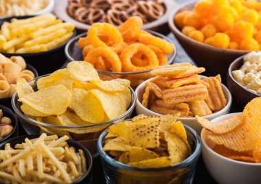 Fıstık, patlamış mısır ve soğan halkaları ve siyah arka planda kase plakaları tuzlu kraker ile tüm klasik patates atıştırmalıkları. Cips ve patates cipsi, nachos ve peynir topları ile cipsler ile Twirls.