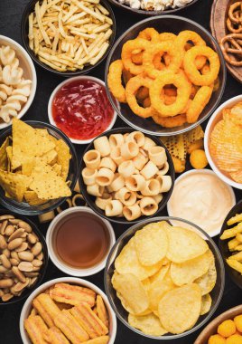 Fıstık, patlamış mısır ve soğan halkaları ve siyah arka planda kase plakaları tuzlu kraker ile tüm klasik patates atıştırmalıkları. Cips ve patates cipsi, nachos ve peynir topları ile cipsler ile Twirls.