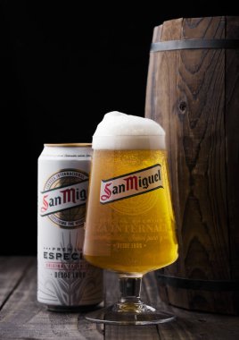 LONDON, UK - APRIL 27, 2018: Aluminium can and original glass of San Miguel lager beer next to wooden barrel.