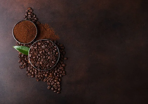 Fresh raw organic coffee beans with ground powder and cane sugar cubes with coffee trea leaf on brown background. — Stock Photo, Image