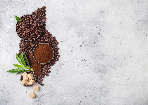 Свежий сырой органический кофе в зернах с молотым порошком и тростниковым сахаром кубики с листьями дерева кофе на светлом фоне кухонного стола . — стоковое фото