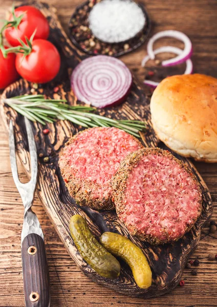 Świeże surowe mielona wołowina hamburgery wołowiny na rocznika deski do krojenia z cebulą bułeczki i pomidory na drewnianym tle. Widok z góry — Zdjęcie stockowe