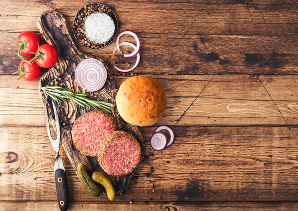 Hamburguesas frescas de carne picada de pimienta cruda sobre tabla de cortar vintage con bollos de cebolla y tomates sobre fondo de madera. Espacio para texto — Foto de Stock