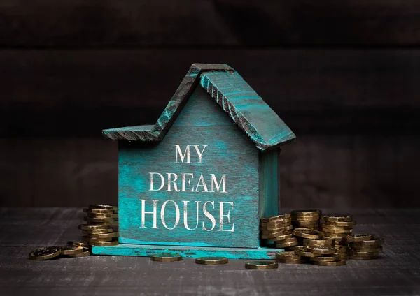 Дерев'яна модель будинку з монетами поруч з нею і рукою — стокове фото