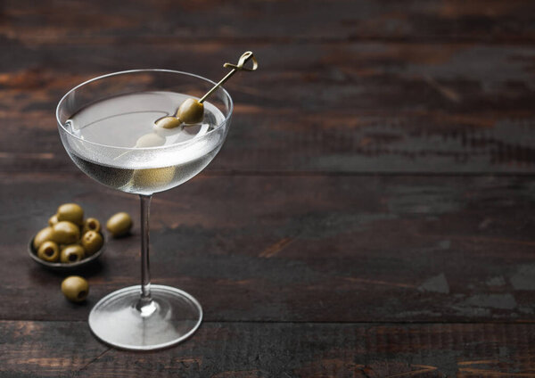 Vodka martini gin cocktail in modern glass with olives in metal bowl and bamboo sticks on dark wooden background. Space for text