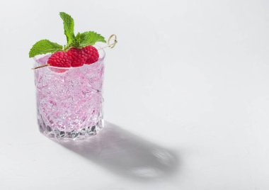 Kristal bardakta pembe limonata kokteyli, beyaz arka planda ahududu, buz ve nane. Koyu gölgeli sert ışık