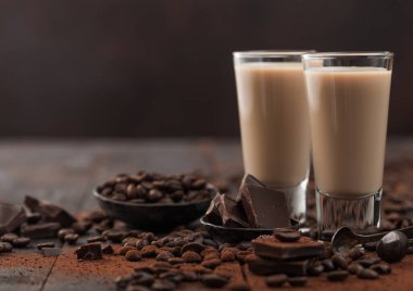 Kahve çekirdekli shot bardaklarında likör ve koyu ahşap arka planda koyu çikolatalı pudra. Metin için boşluk