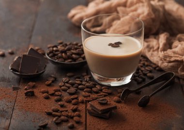 Bir bardak İrlanda kremalı baileys likörü, buzlu kahve çekirdekleri ve koyu ahşap arka planda koyu çikolata ve kahverengi kumaşlı toz. Metin için boşluk